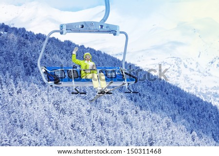 Happy skier young woman sit on the ski lift and waiving hand