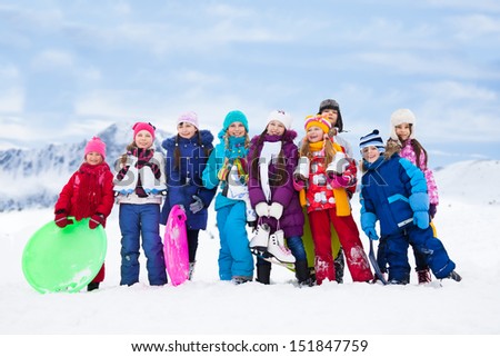 Group of kids together outside in snow with sled, ice skates having fun with winter activities