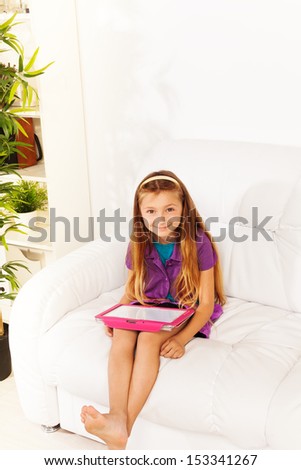 Little beautiful Caucasian girl reading from tablet computer sitting with on coach