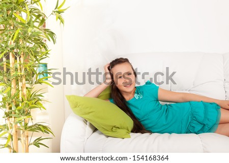 Happy nice  little girl 10 years old laying hugging pillow on the white coach in living room at home