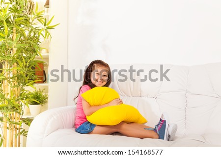 One happy calm and relaxed Asian little girl 5 years old sitting with pillow on the white leather coach in living room at home