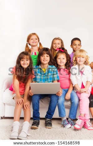 Group of happy little kids, boys and girls sitting on the coach with laptop in living room