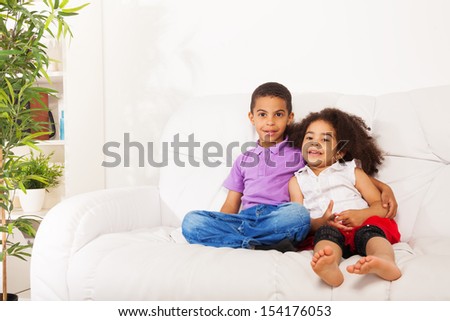 Brother and sister siblings sitting and hugging on the couch at home interior