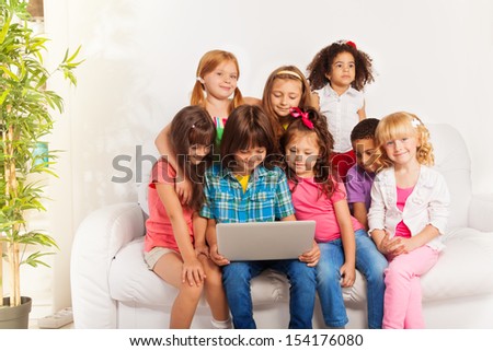 Large group of kids sitting occupied on the couch with laptop, looking at screen and smiling