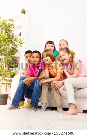Group of happy kids singing together sitting on the coach in living room