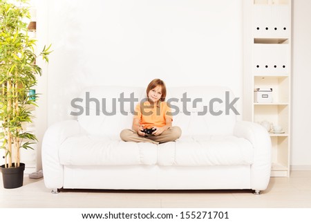 Happy smiling Caucasian boy gamer playing video games holding game controller sitting on the white sofa in living room