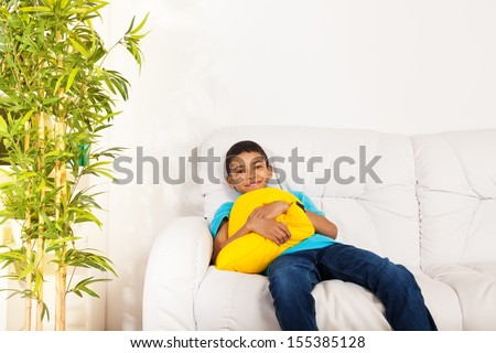 One happy black smiling boy 10 years old sitting with vivid yellow pillow sitting on the white leather coach in living room at home