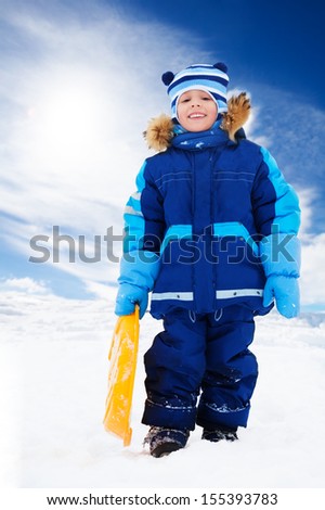 Happy 5 years old Caucasian boy standing holding sled, on snow outside in winter