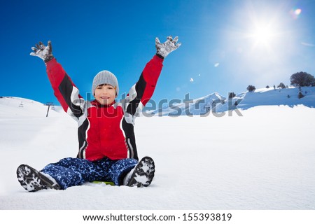 Happy exited boy sitting on sled with her hands lifted,, in the mountains