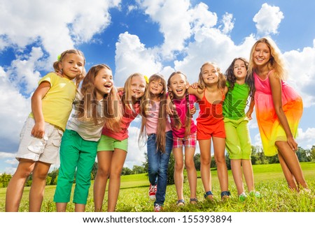 Many happy girls standing in a row in the park on the green grass on sunny summer day, hug and bend to camera