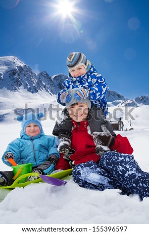 Three happy brothers sitting in snow park outside in winter