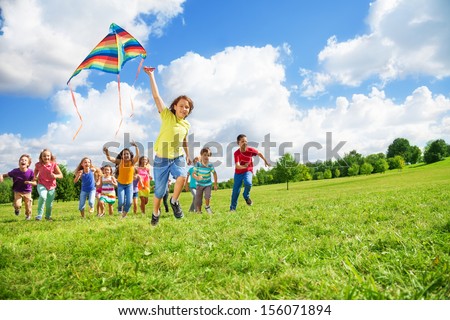 Boy Running With Kite With Large Group Of Friends, Boys And Girls Running After