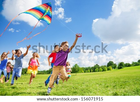 Dynamic Composition Of Kids Boys And Girls Run With Kite In A Large Group Together In The Park On Summer Day