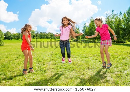 Three girls jumping over the rope in the park, having fun in active games outside