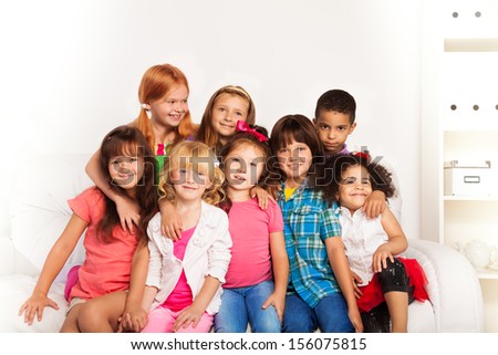 Group of little kids sitting on a couch and smiling, hugging together at home interior