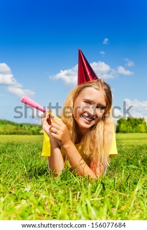 Beautiful little girl with noisemaker horn and birthday party cap laying outside with happy expression on sunny summer day