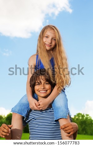 Two kids, boy carry girl on his back, both happy and smiling, in the park on sunny summer day