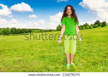 Beautiful happy smiling girl 11 years old in green shirt standing in the park jumping over the rope