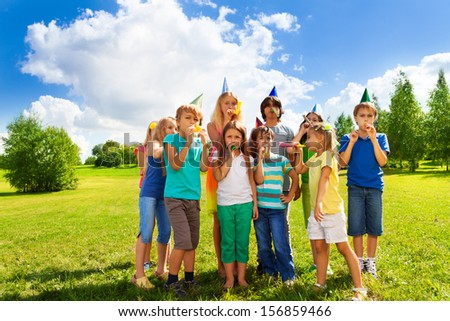 Large group of happy kids outside on a birthday party blowing noisemakers horns  and twisted whistles