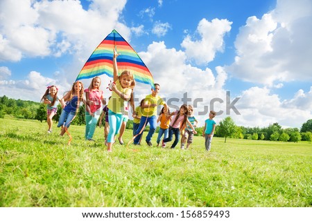 Little cute girl running with kite on a sunny day in the park with many friends in the park