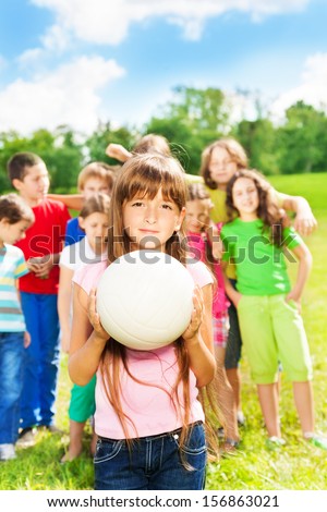 Nice little girl with the ball standing in the park with her team behind her
