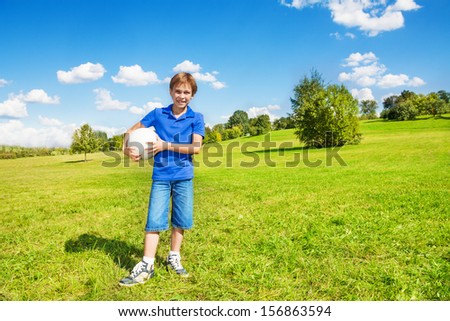 Nice smiling happy 8 years old boy stand with volleyball ball in the park field outside on sunny summer day