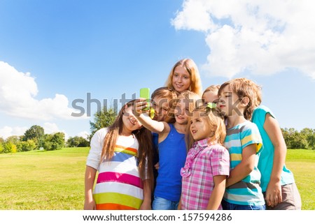 Group of happy kids taking picture of friends with smartphone standing together in the park