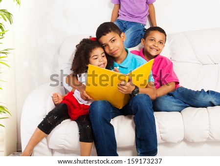 Family, group of four kids with older brother reading books to brothers and sister hugging little girl