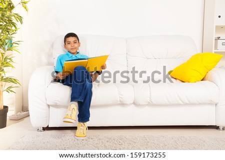 10 years old black boy sitting on the sofa and reading book in living room at home