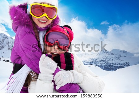 Two cute kids friends girls hugging with skis and mountain on background