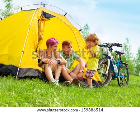 Young couple sitting in the tent with little boy drinking tea with bikes standing near