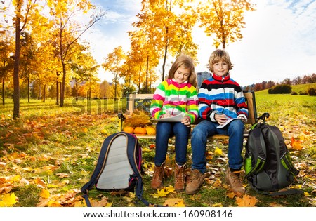 Portrait of two happy blond kids, twins brother and sister sitting on the bench after school