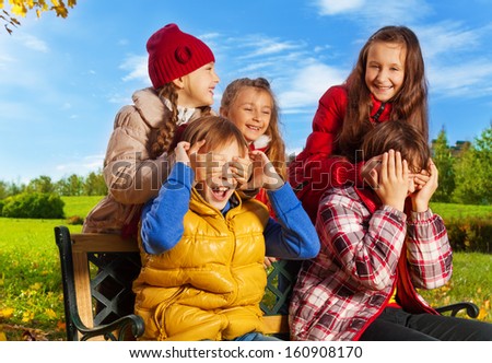 Friends and surprise guess who action with girls hiding boys face with palms in autumn park