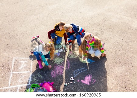 Group of four boys and girls, friends in autumn clothes painting with chalk on the asphalt