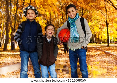 Three black boys, brother 5 8 10 years old standing with basketball ball in autumn park with orange maple trees smiling and laughing