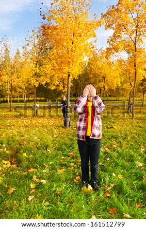 Kids play hide and seek with boy counting covering face with palms while others hiding behind autumn male trees