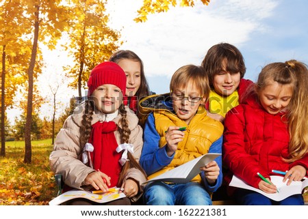 Group of five kids around 10 years old drawing images sitting outside in autumn day