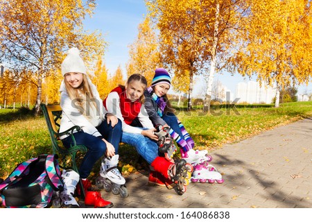 Three happy girls putting on roller blades sitting in the park