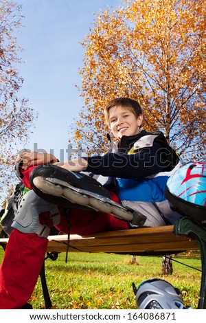 10 years old boy sitting on the bench in autumn park with roller blades shoot from low angle