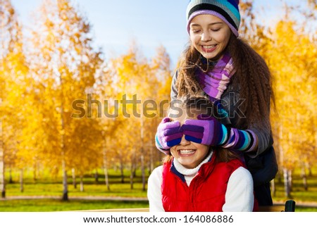Close portrait of two happy school age happy smiling girls playing guessing who am I covering eyes with palms