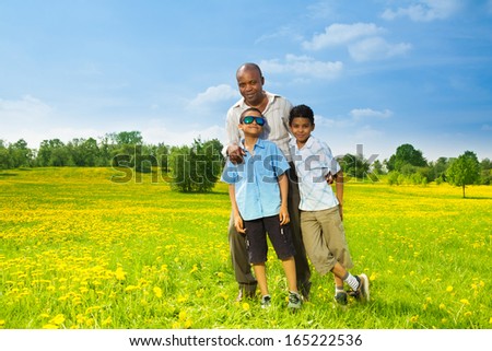 Happy black father with his sons standing on the lawn in the park on sunny day
