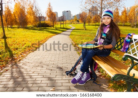 Cute 11 years old girl in warm clothes in the park sitting on the bench in autumn park
