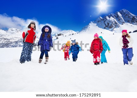 Large group of kids in bright colorful clothes walking on snow plane in the mountains