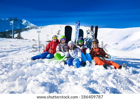 Happy friends sitting with snowboards and skis