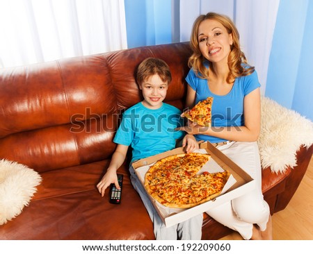 Happy boy and mother eating pizza on the couch