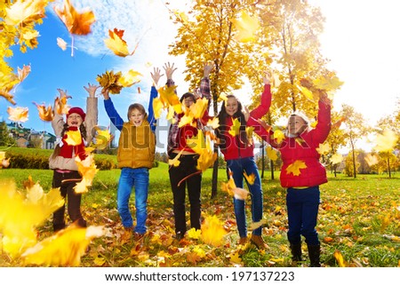 Group of five kids, boys and girls throwing autumn maple leaves in the park on sunny day