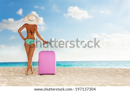 Beautiful tall woman with big pink suitcase standing on the white sand beach