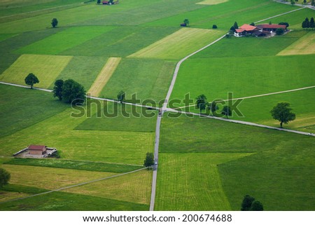 Areal photograph of read crossing, green fields stripes, trees and houses near Neuschwanstein castle in Germany