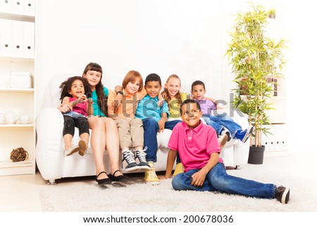 Large group of diversity looking kids sitting on the couch at home, hugging, smiling and laughing