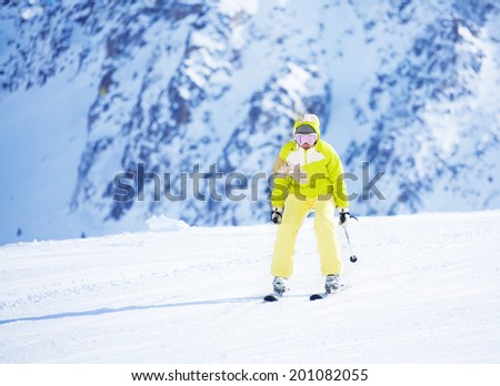 Happy young woman skier in bright clothes going downhill with mountain wall on background